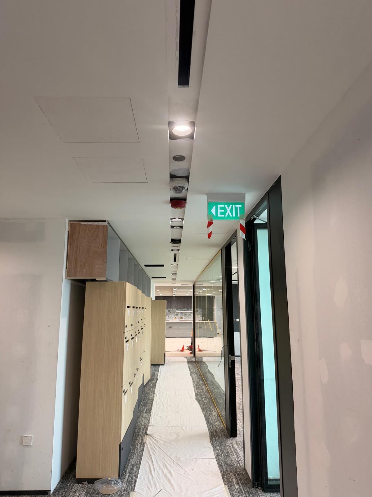 Corridor with recessed lighting, emergency exit sign and ceiling services installed by Shanteck SG Engineering