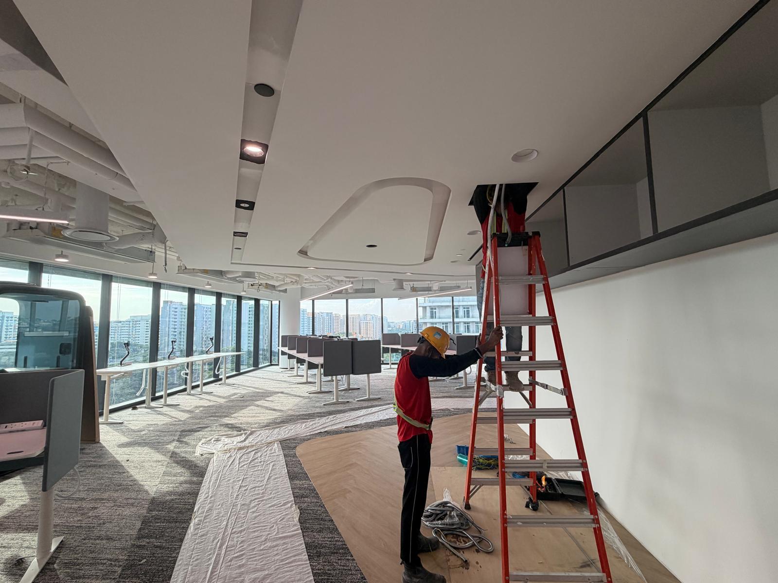 Technician installing ceiling light fittings and FCU access in a Singapore office fit-out