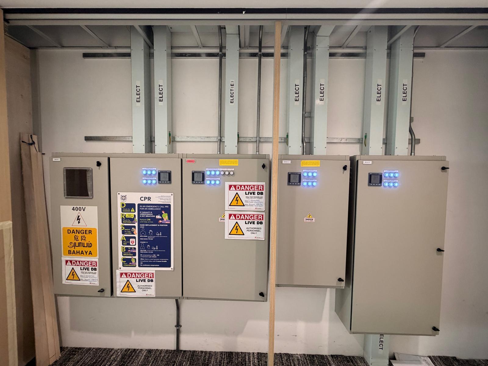 Bank of 400V distribution boards with energy meters, live DB safety signage and steel conduit risers — licensed electrical installation Singapore