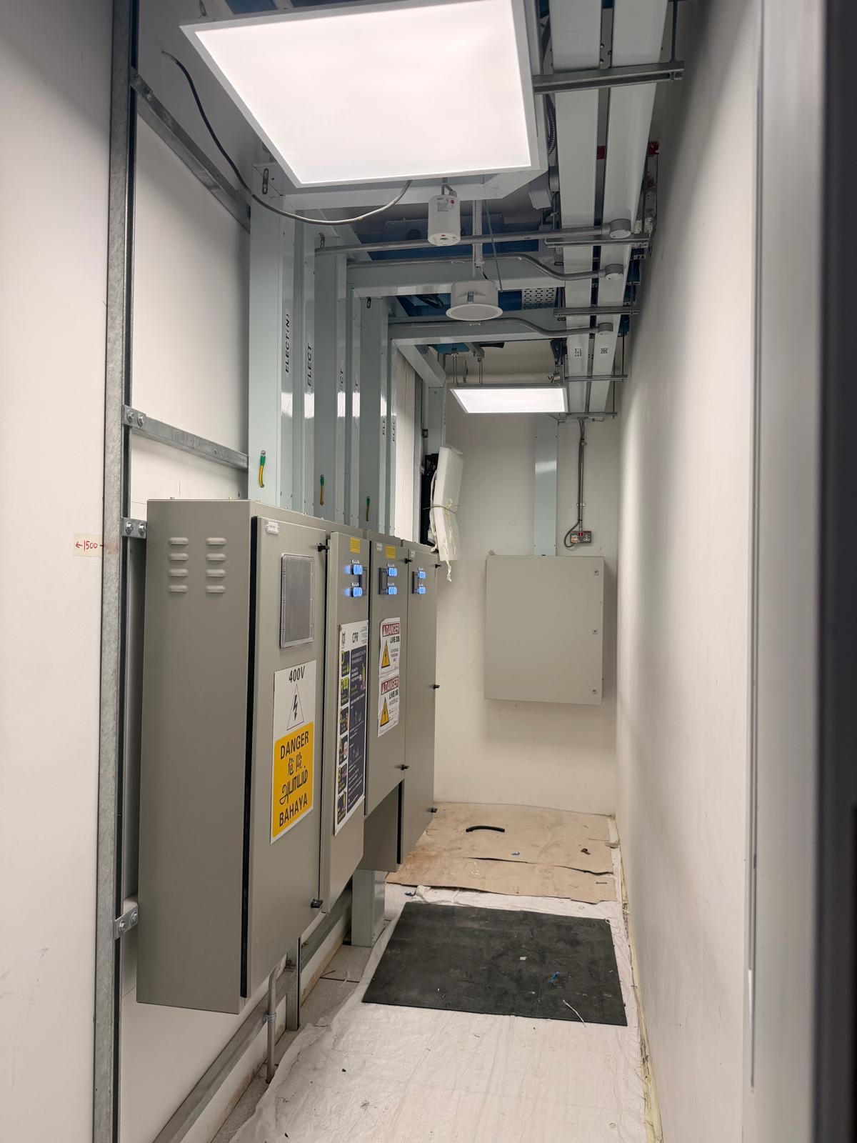 Electrical riser room with 400V main distribution boards, danger signage and steel conduit containment in Singapore